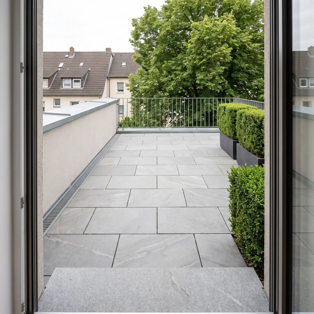 Dachterrasse mit großformatigen Platten auf Stelzlagern, umlaufender Bepflanzung und Blick über die Nachbarbebauung